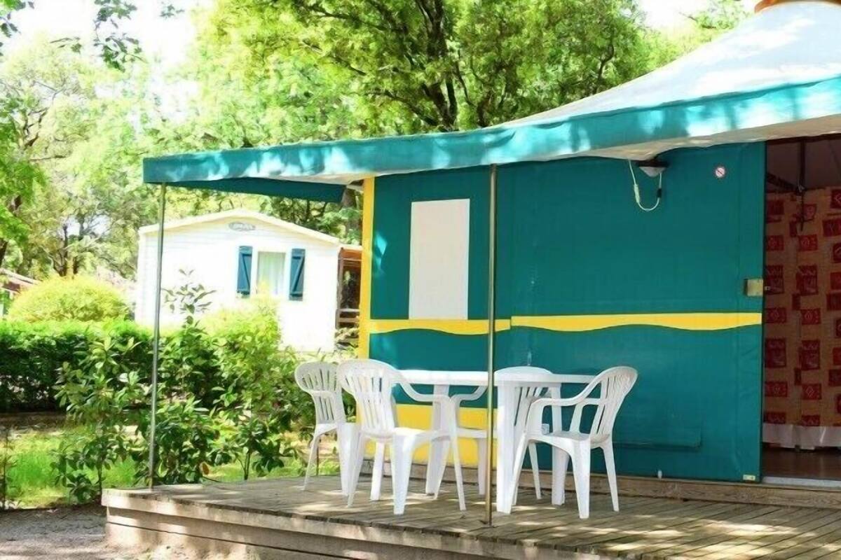 A small, colorful tent with a table and chairs outside, surrounded by greenery.