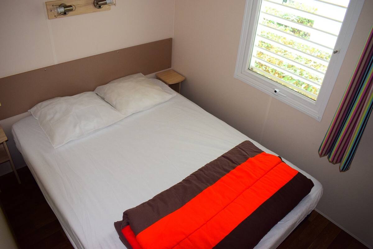 A bed with white bedding, a brown headboard, and a red and brown blanket.