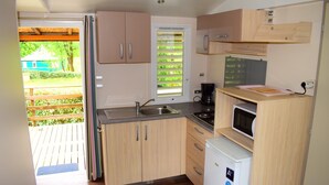 Una cocina compacta con armarios de madera, un lavamanos, un microondas y un refrigerador pequeño.
