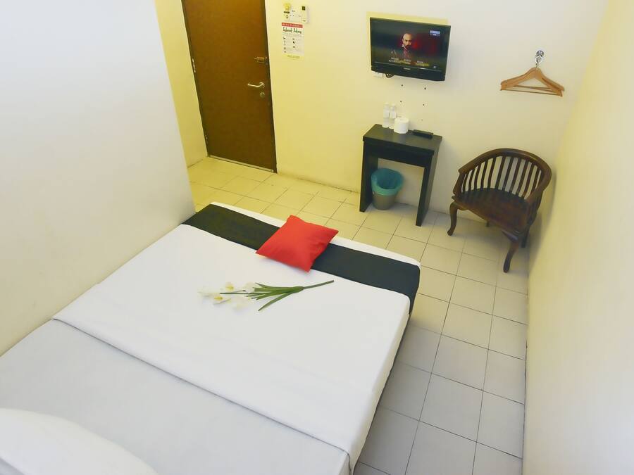 A hotel room with a bed, a small table with toiletries, a chair, and a TV on the wall.