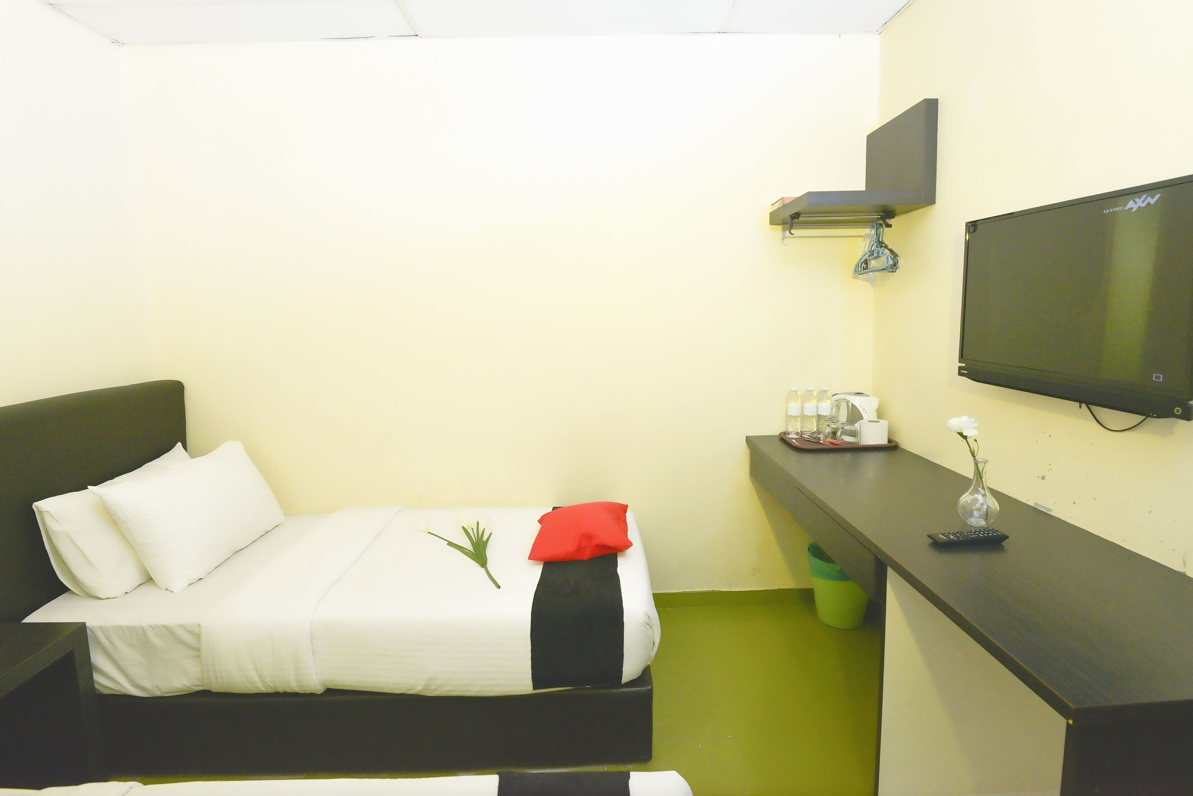 A small hotel room with a bed, a desk, a TV, and a green trash bin.