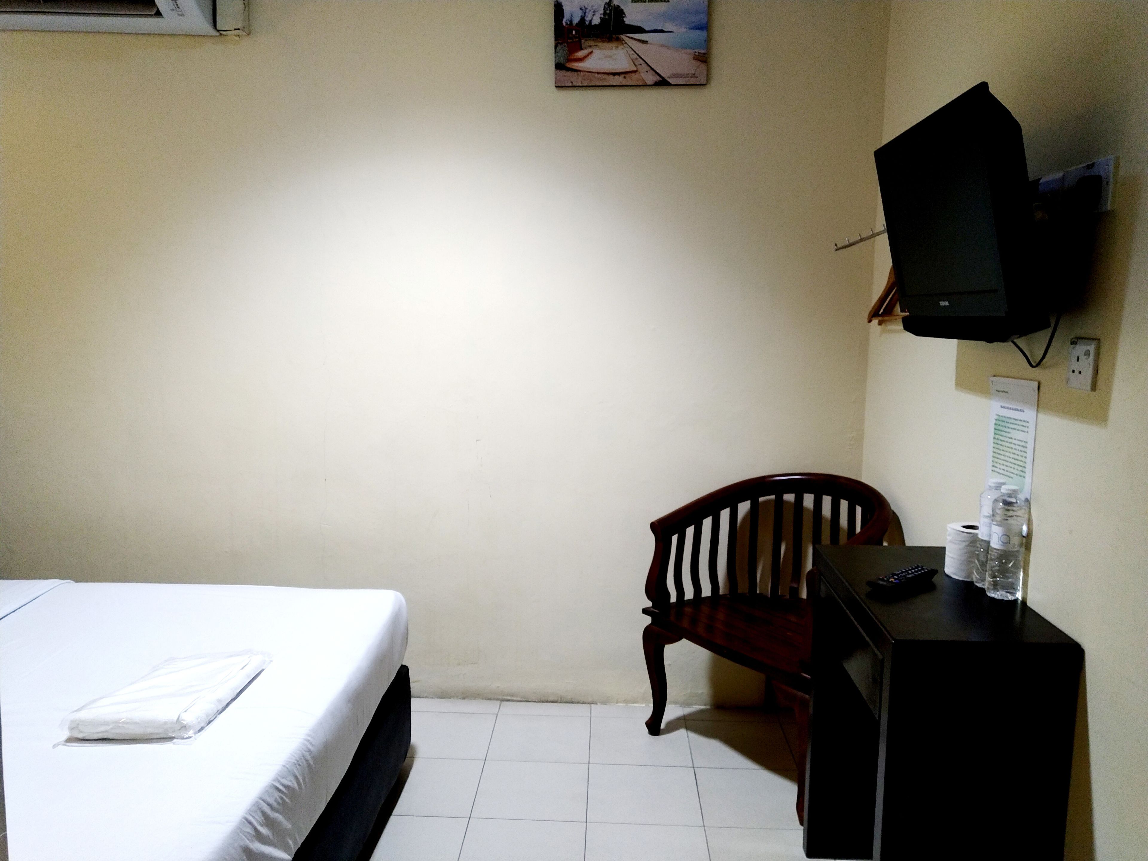 Ein Hotelzimmer mit einem Bett, einem Holzstuhl, einem Schreibtisch mit Fernseher und einem Wandbild.
