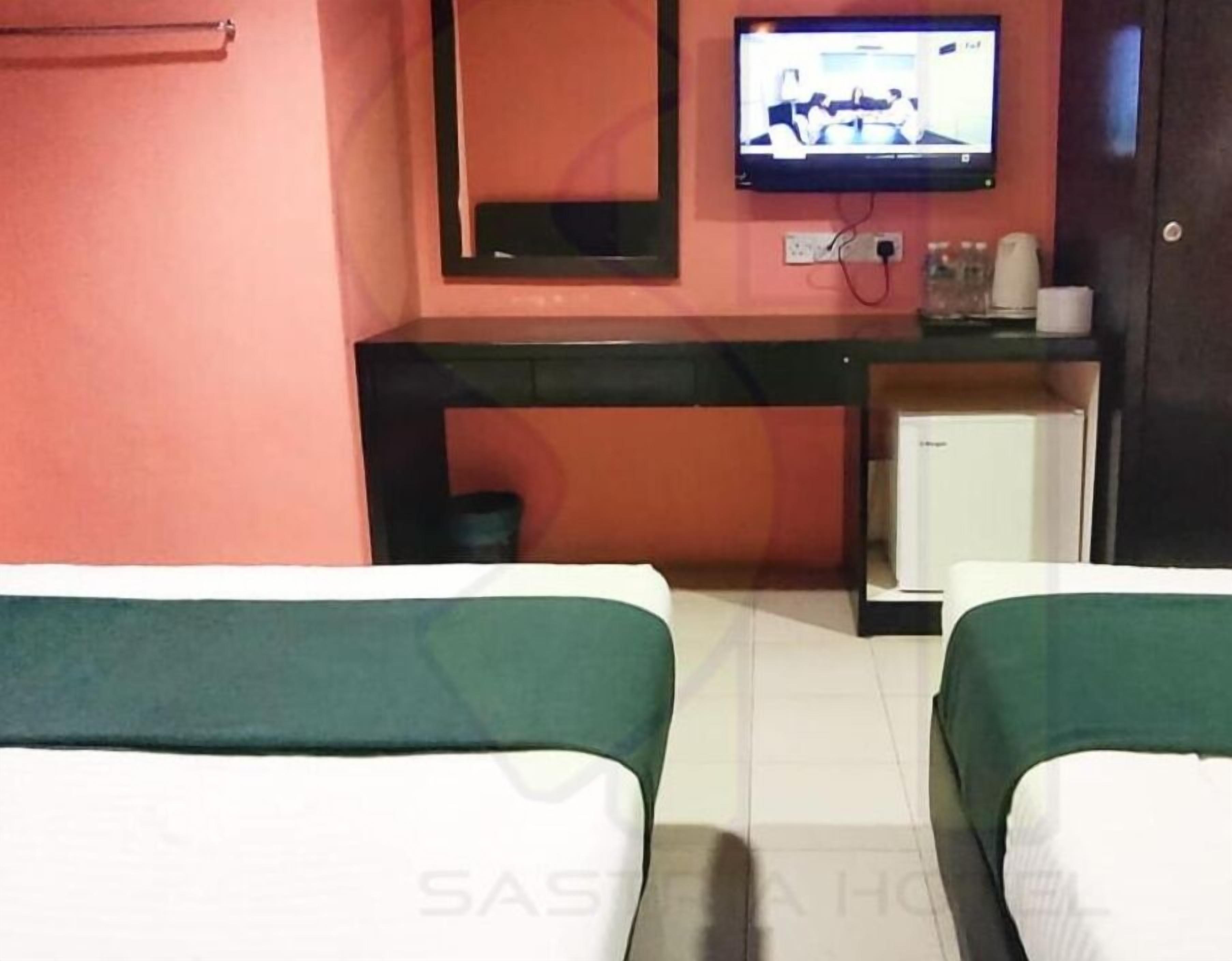 A hotel room with two beds, a small desk with a television, and a mirror on the wall.