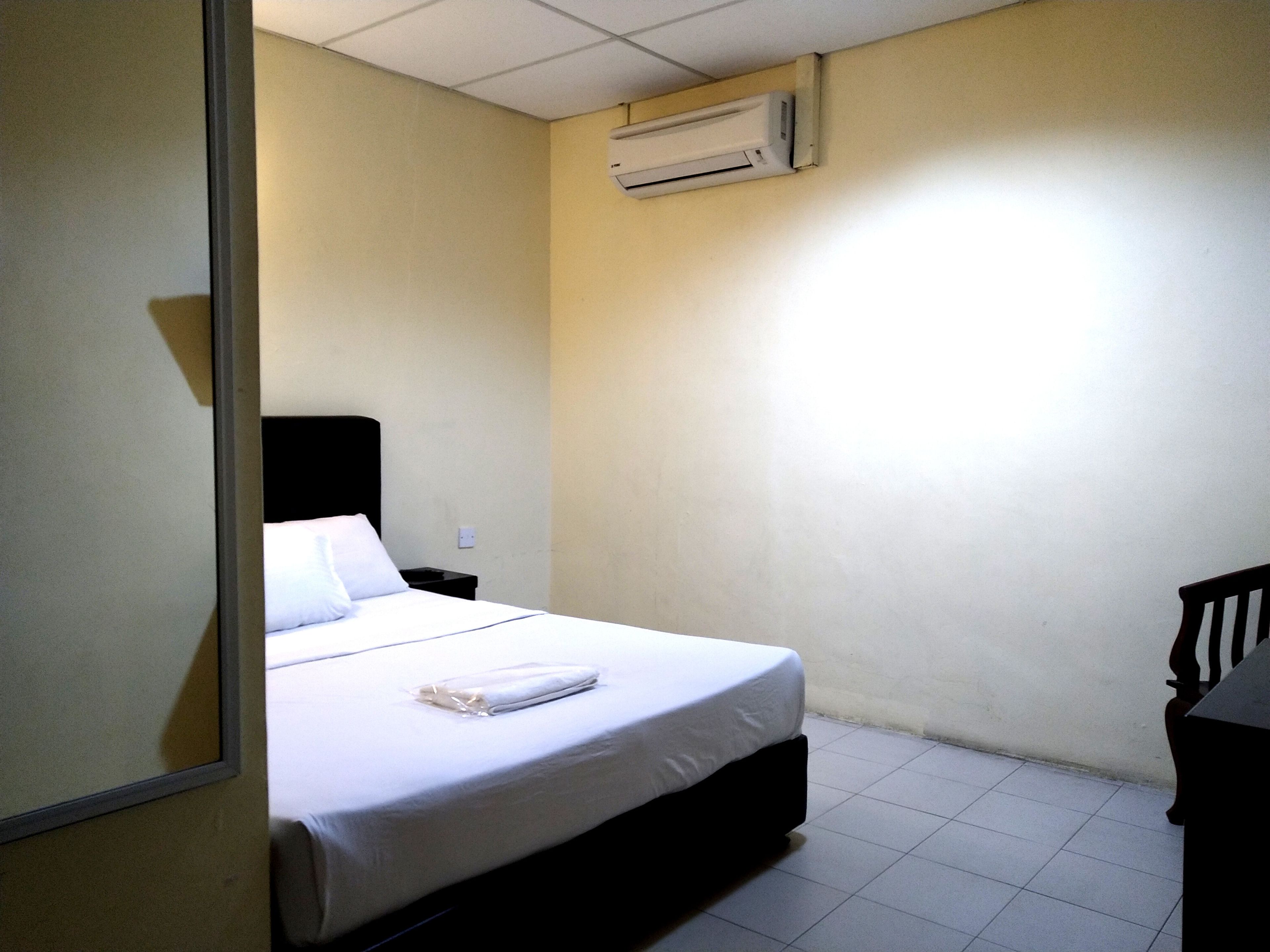 A small, clean room with a single bed, a nightstand, a chair, and an air conditioning unit on the wall.