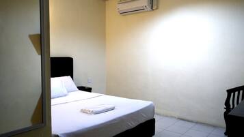 Una habitación pequeña y limpia con una cama individual, una mesita de noche, una silla y un equipo de aire acondicionado en la pared.