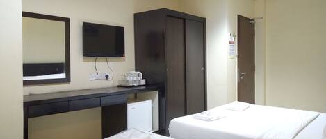 A hotel room with two beds, a desk with a mirror, a wardrobe, and a small kitchenette area.