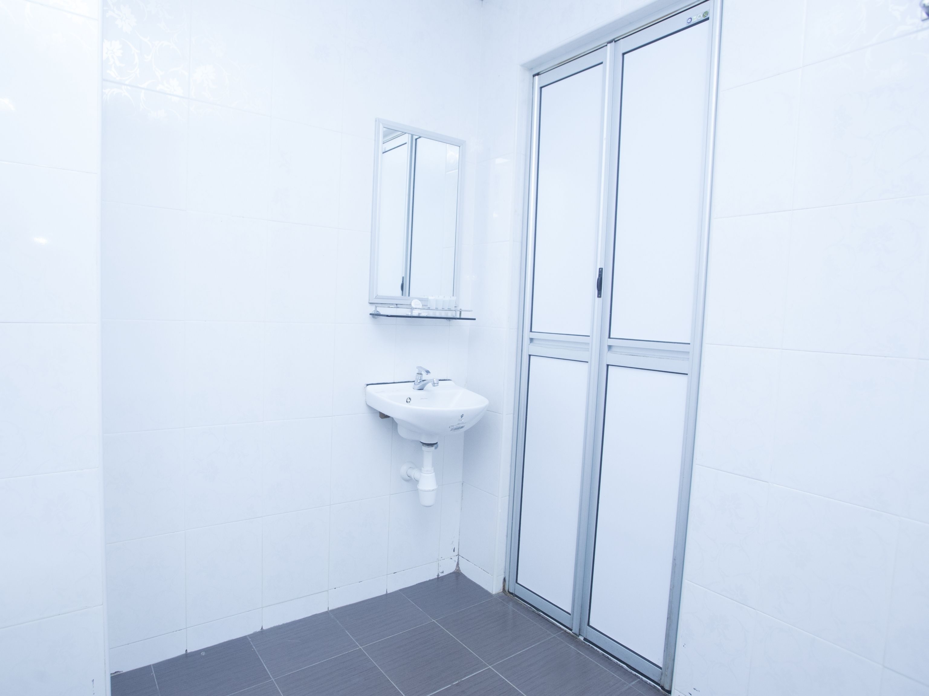 A bathroom with white tiles, a sink, a mirror, and a glass shower door.