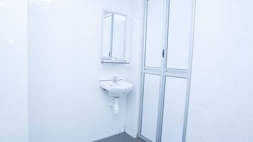 Un bagno con piastrelle bianche, un lavandino, uno specchio e una porta doccia in vetro.