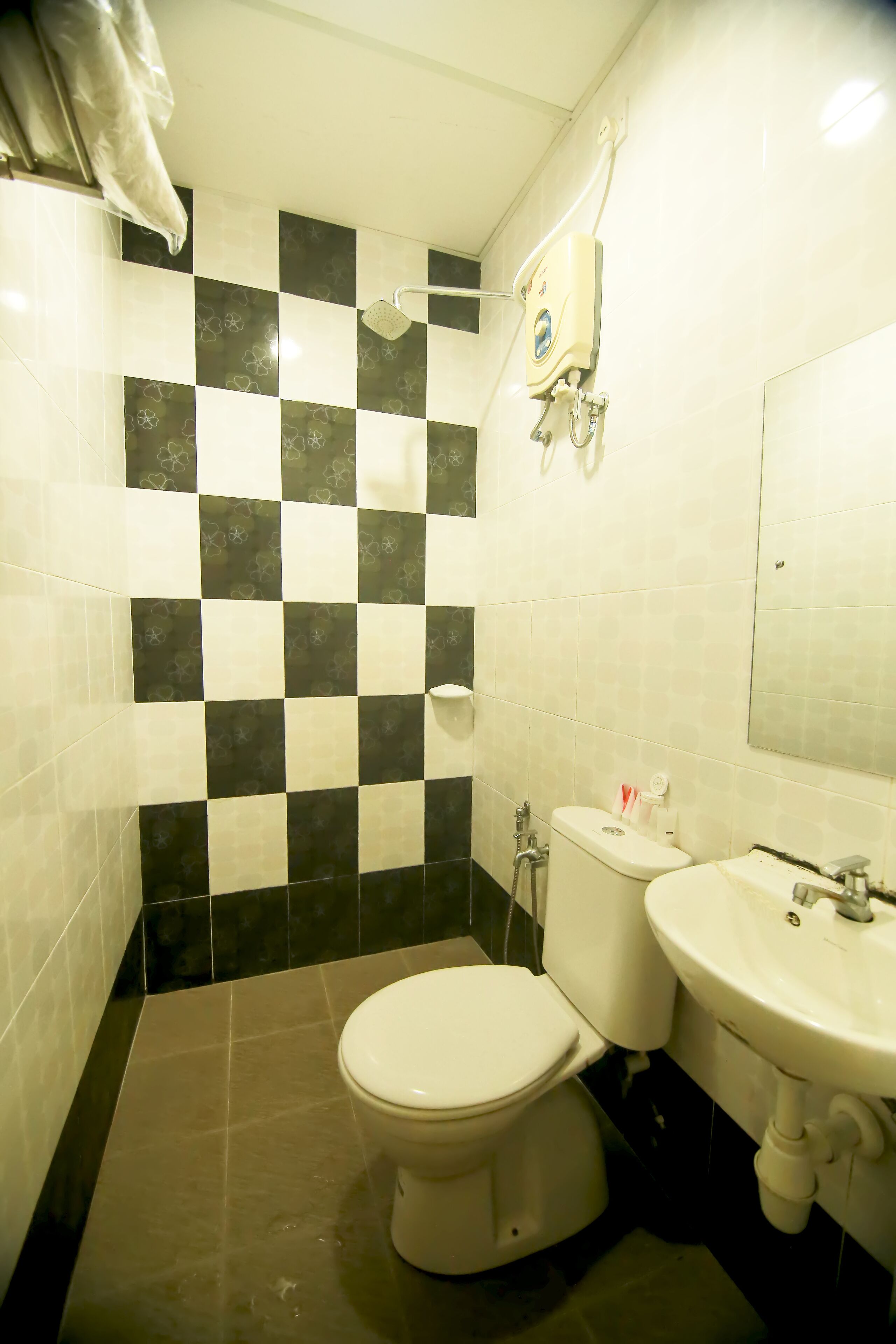 A bathroom with a checkered tile wall, a toilet, a sink, and a showerhead.