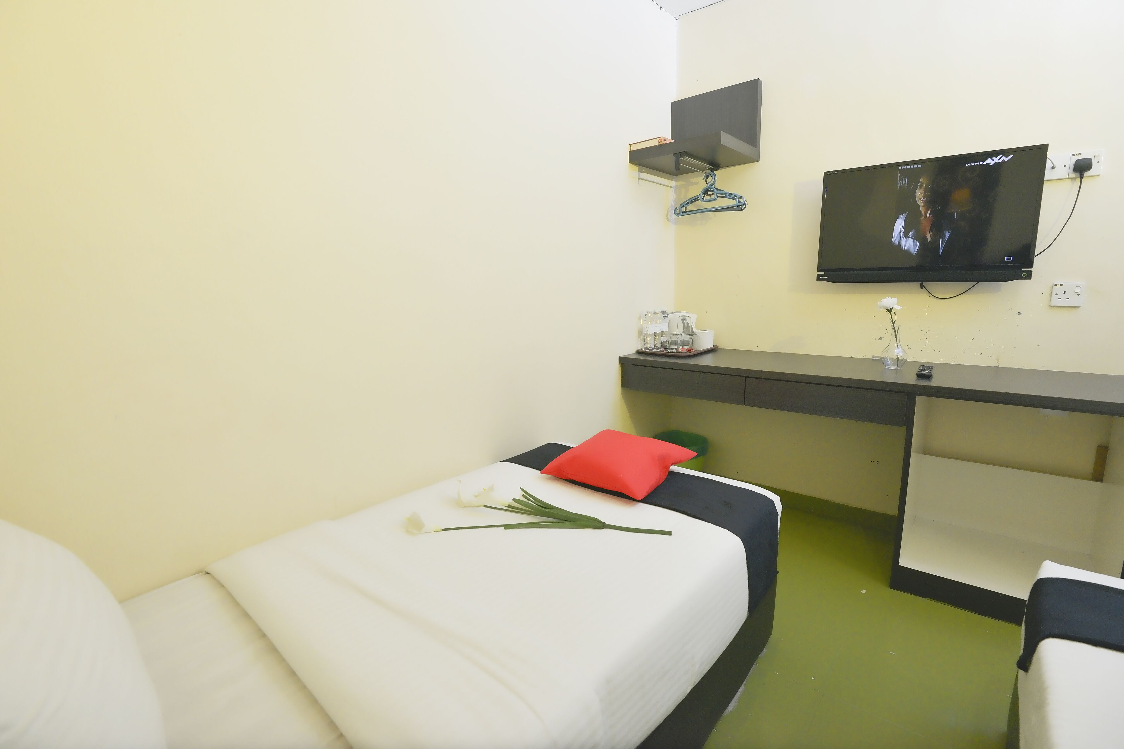 Habitación de hotel con dos camas, televisión, una mesita con un florero y piso verde.