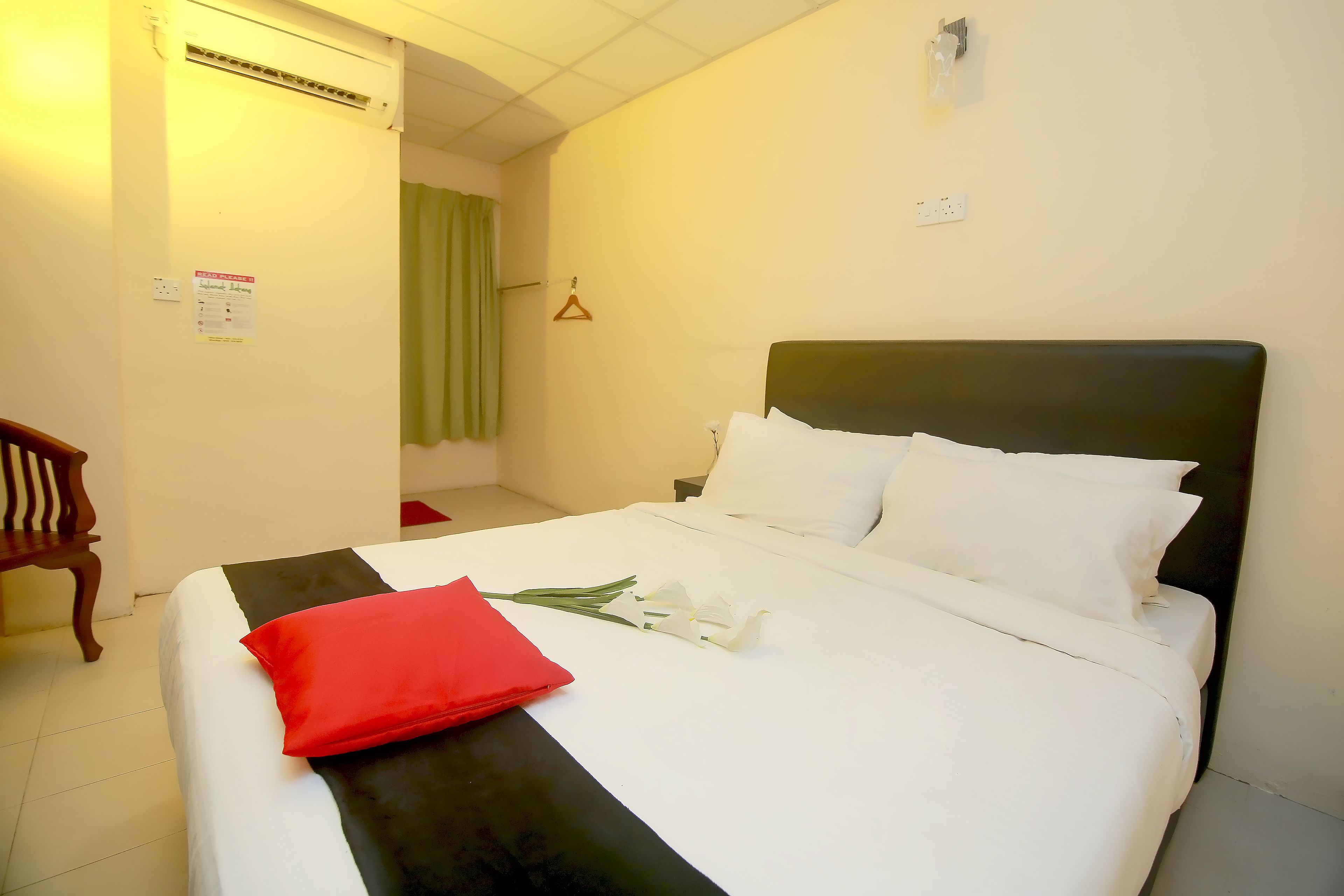 A neatly made bed with white and black bedding, a red pillow, and white flowers.
