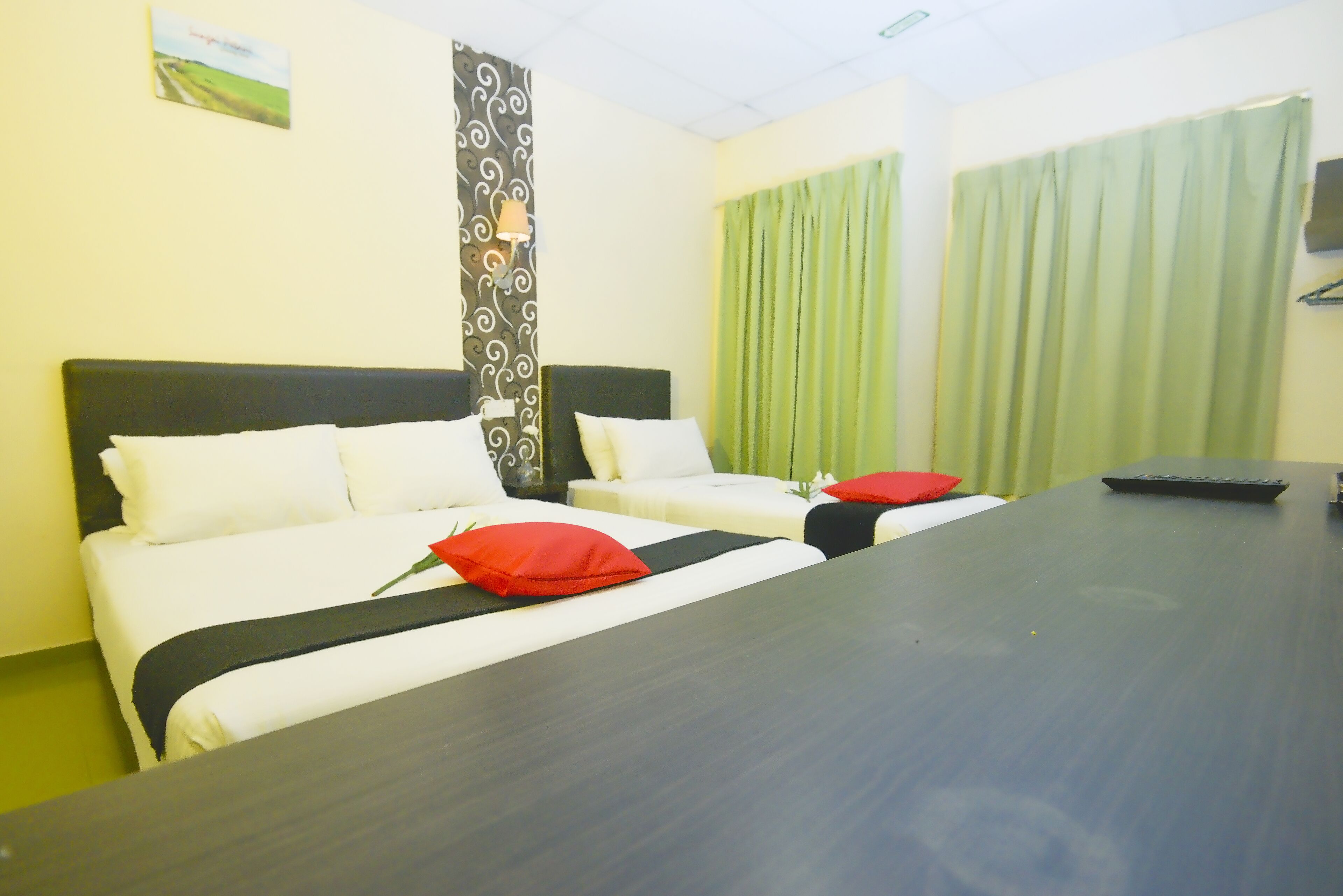 Habitación de hotel con dos camas, un escritorio y una cortina verde.