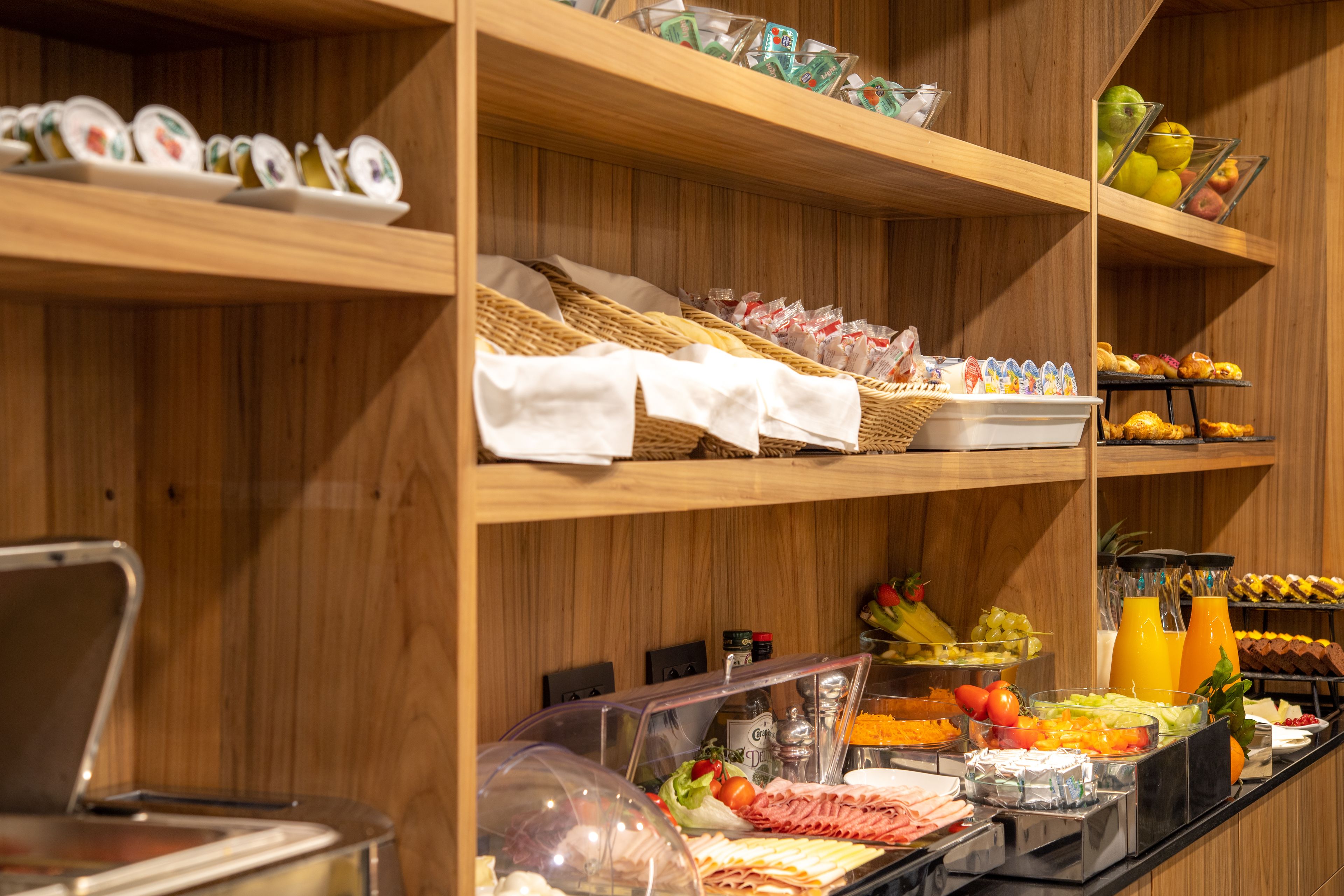 A buffet with various food items and beverages, including fruits, vegetables, and prepared dishes, displayed on wooden shelves.