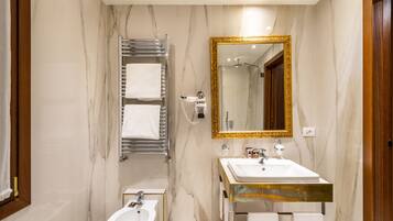 A bathroom with a marble wall, a gold-framed mirror, a white sink, and a towel rack.