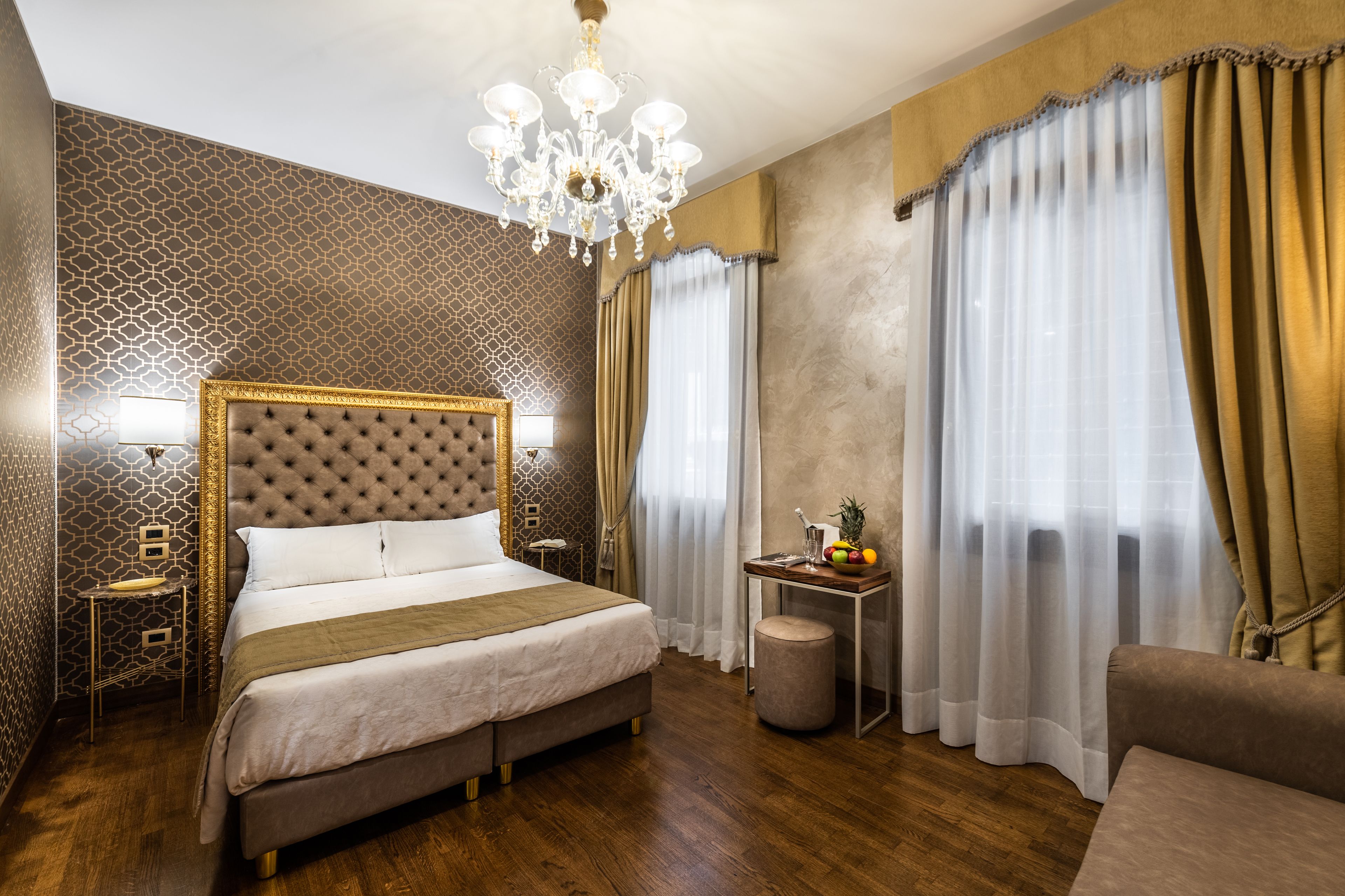 Habitación de hotel elegante con una cama grande, un candelabro, una pequeña mesa con fruta y cortinas.
