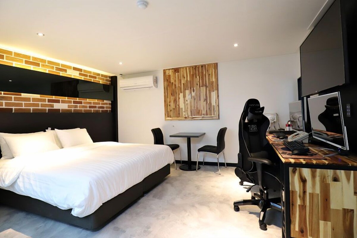 A modern hotel room with a large bed, a desk with a computer, and a chair.
