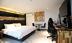 A modern hotel room with a large bed, a desk with a computer, and a chair.