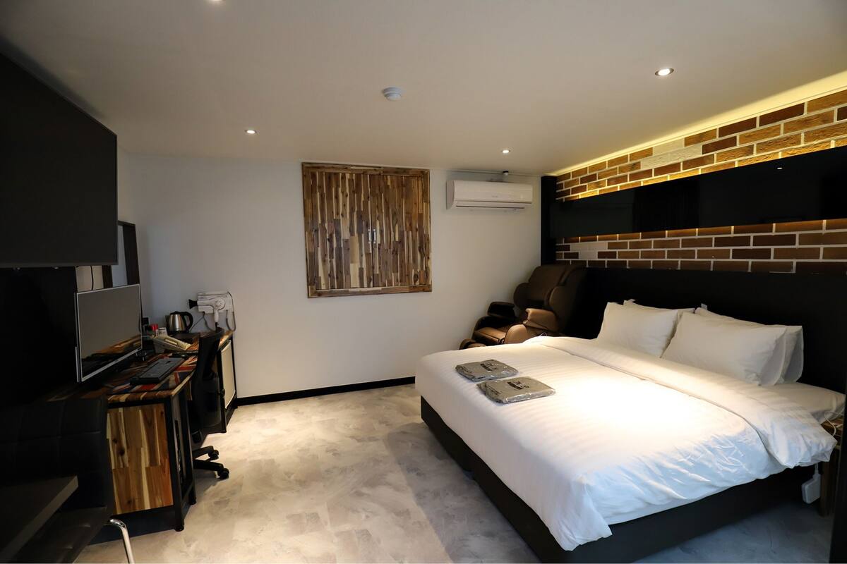 Una habitación de hotel moderna con una cama grande, un escritorio con computadora, un televisor de pantalla plana y una pared decorativa de ladrillo.