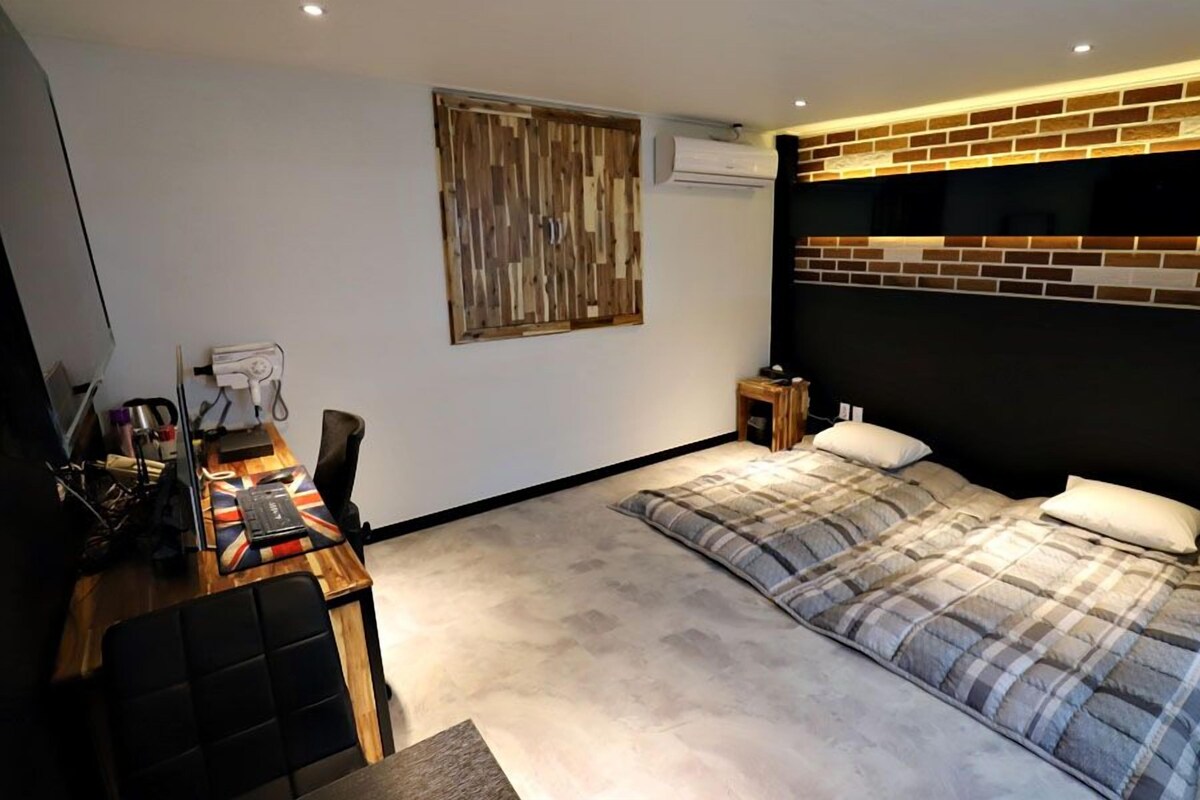 A bedroom with a bed, a desk with a computer, a chair, and a wall-mounted air conditioner.