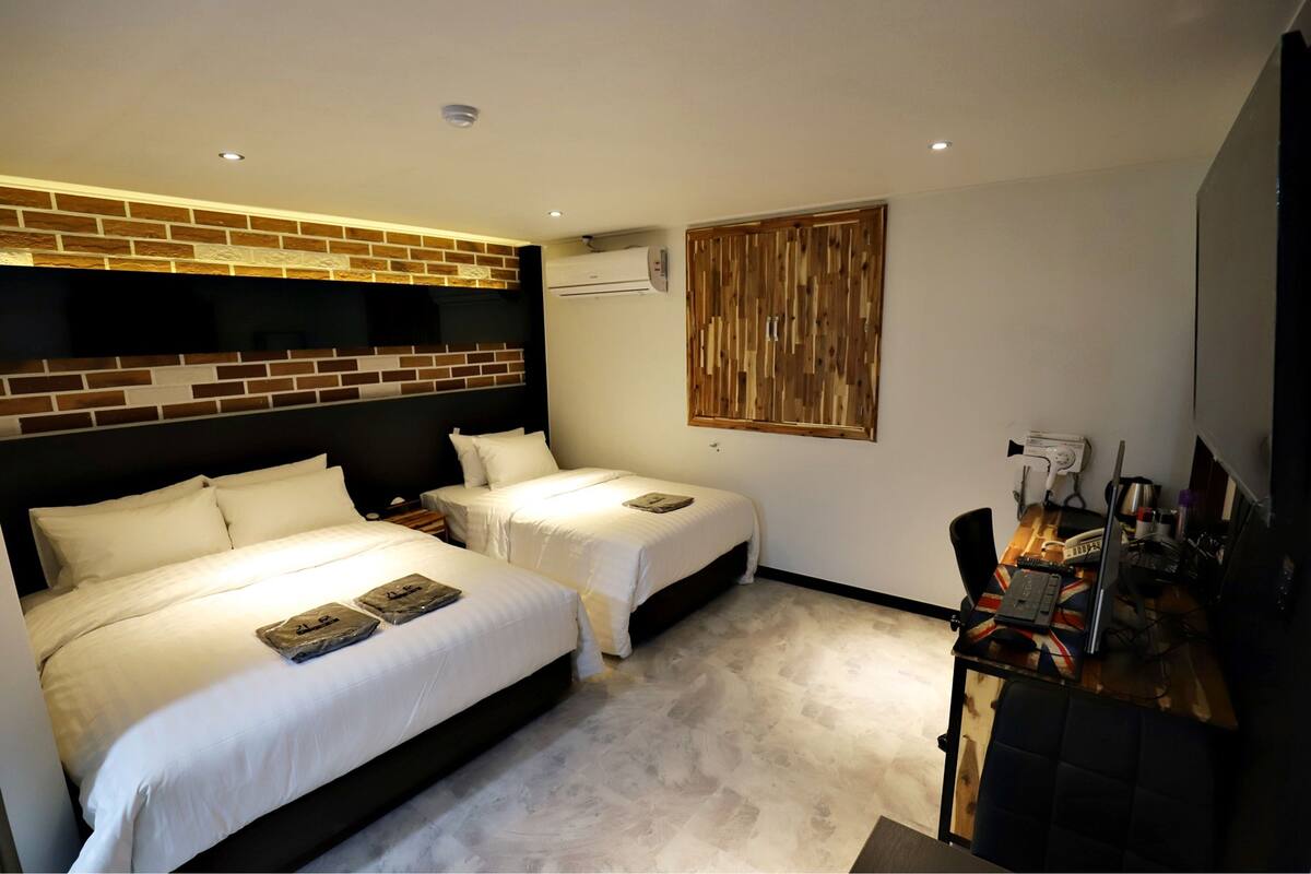 Habitación de hotel con dos camas, un escritorio con una computadora portátil y un aire acondicionado de pared.