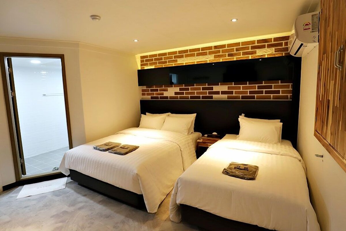A hotel room with two beds, a sliding glass door, a brick accent wall, and a built-in air conditioning unit.
