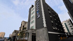 Un hotel moderno con un llamativo letrero vertical, varios pisos y un área de estacionamiento.