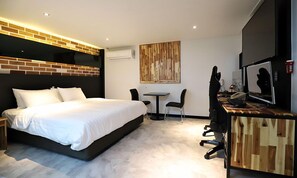 A modern hotel room with a large bed, a desk with a computer, a chair, and a television.