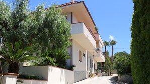 A two-story building with a balcony, surrounded by lush greenery and a clear sky. - B&B La Piccola Oasi (Motta San Giovanni)
