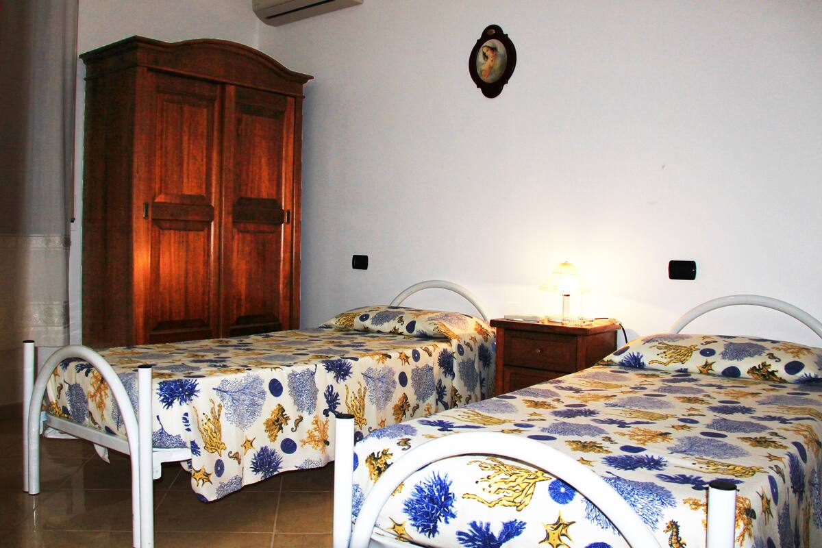 Un dormitorio con dos camas individuales, un armario de madera, un aire acondicionado y un cuadro en la pared.