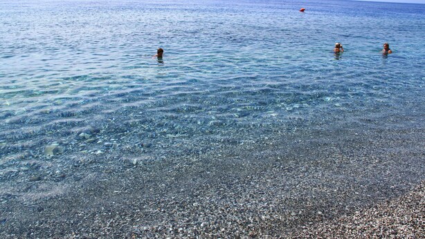 A beach with clear water and pebbles, three people swimming, and a distant boat. - B&B La Piccola Oasi (Motta San Giovanni)