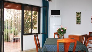A dining area with a table set for four, a TV mounted on the wall, and a window with curtains. - B&B La Piccola Oasi (Motta San Giovanni)