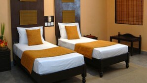 A hotel room with two single beds, each with a white mattress and a brown bedspread. There are wooden headboards and a small wooden nightstand between the beds. - Heritage Habarana Resort (Habarana)