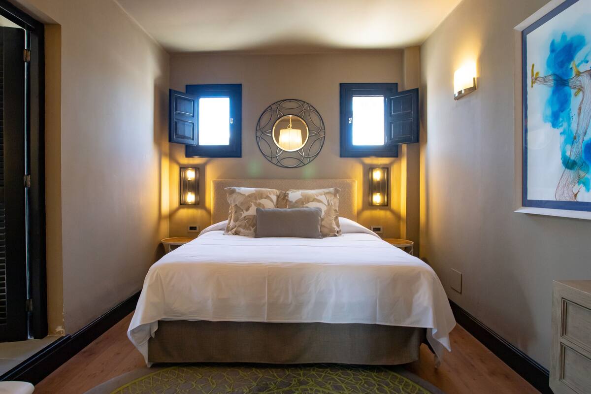 Ein Hotelzimmer mit einem großen Bett, zwei Wandlampen, einem dekorativen Spiegel und einem Bild an der Wand.