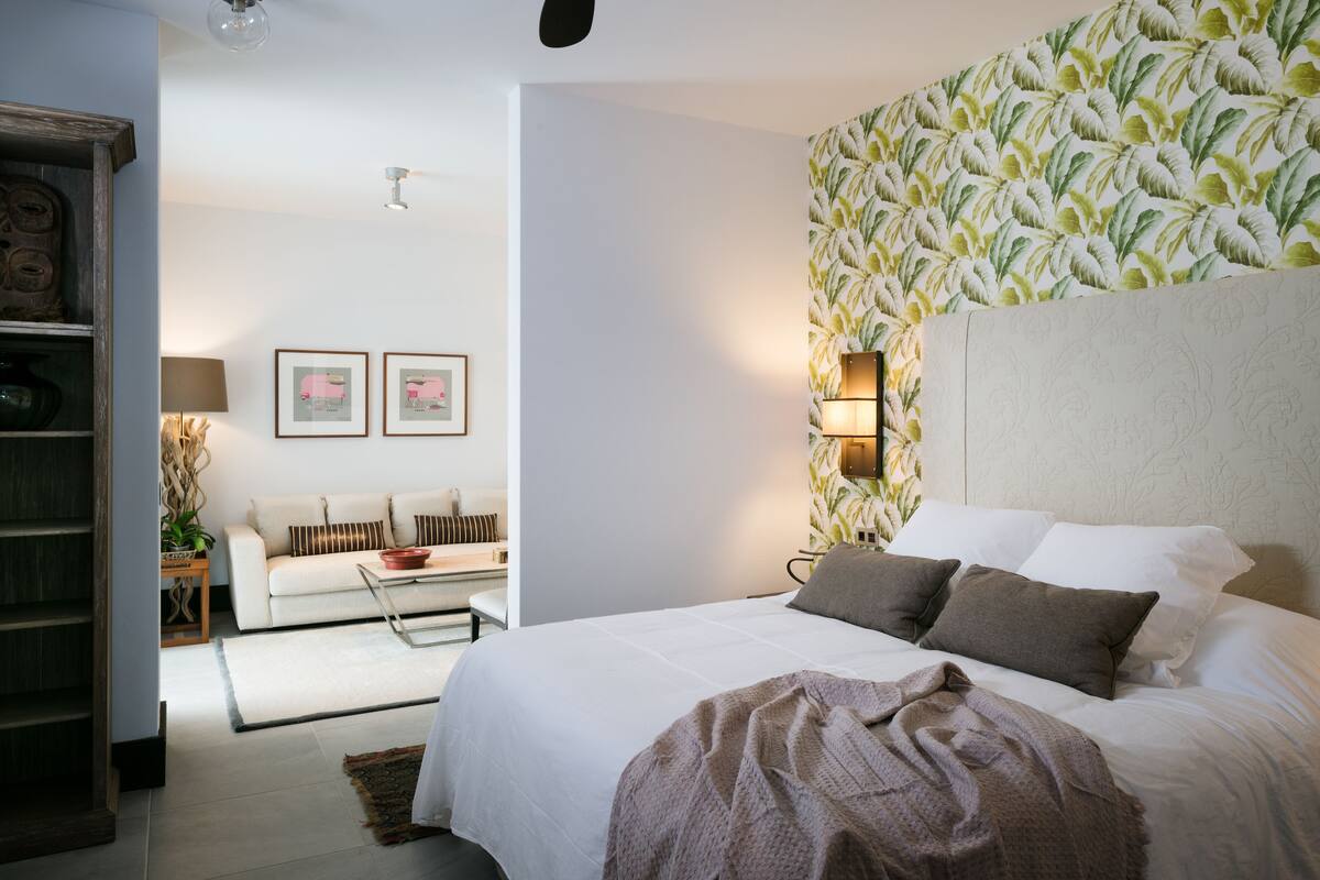 Ein Schlafzimmer mit einem großen Bett, einem Nachttisch, einer Lampe und einer Wand mit Blättermuster.