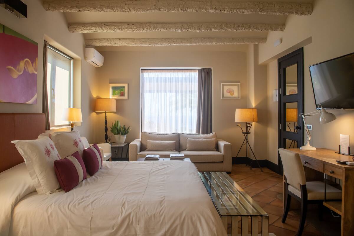 Ein Hotelzimmer mit einem großen Bett, einem Schreibtisch, einem Sessel, einer Couch und einem Fernseher.