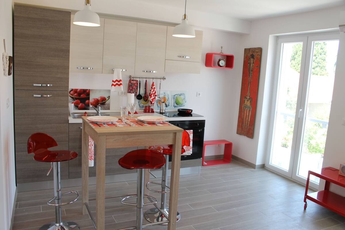 A modern kitchen with wooden cabinets, a central island with stools, and a red accent wall.