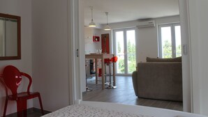 A modern living room with a red chair, a sofa, and a dining area with a table and chairs. - Apartments Mala (Konavle)
