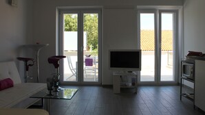 A modern living room with a sofa, a glass coffee table, a flat-screen TV, and a sliding glass door leading to an outdoor area. - Apartments Mala (Konavle)