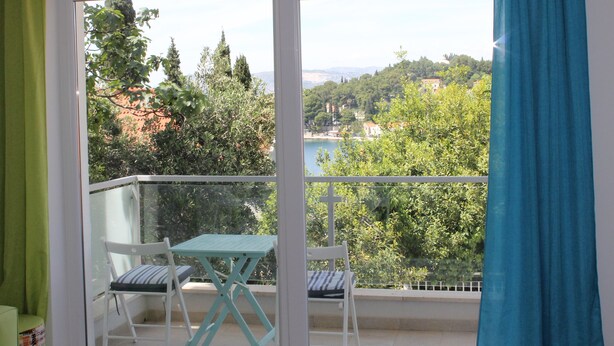 A balcony with a table and two chairs, overlooking a scenic view of trees and buildings. - Apartments Mala (Konavle)