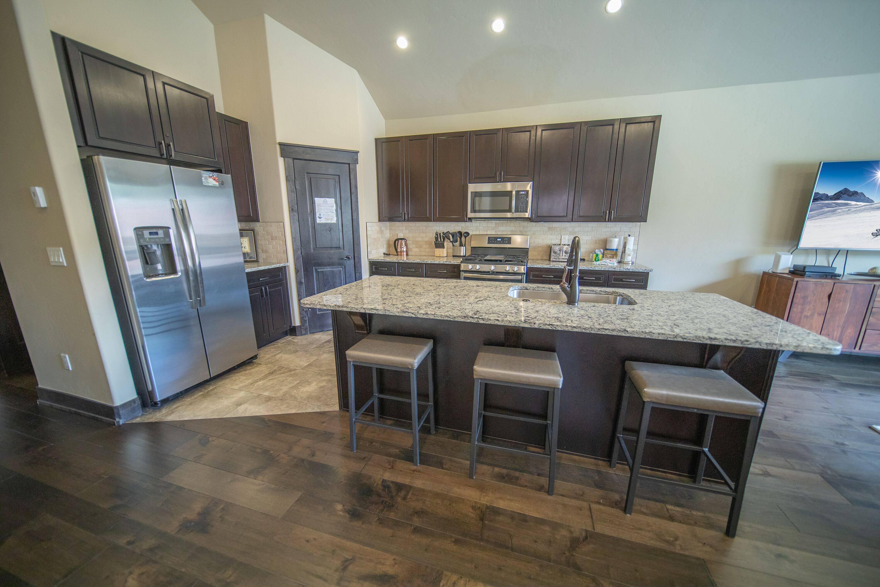 A modern kitchen with dark wood cabinets, stainless steel appliances, a granite countertop, and a built-in island with bar stools.