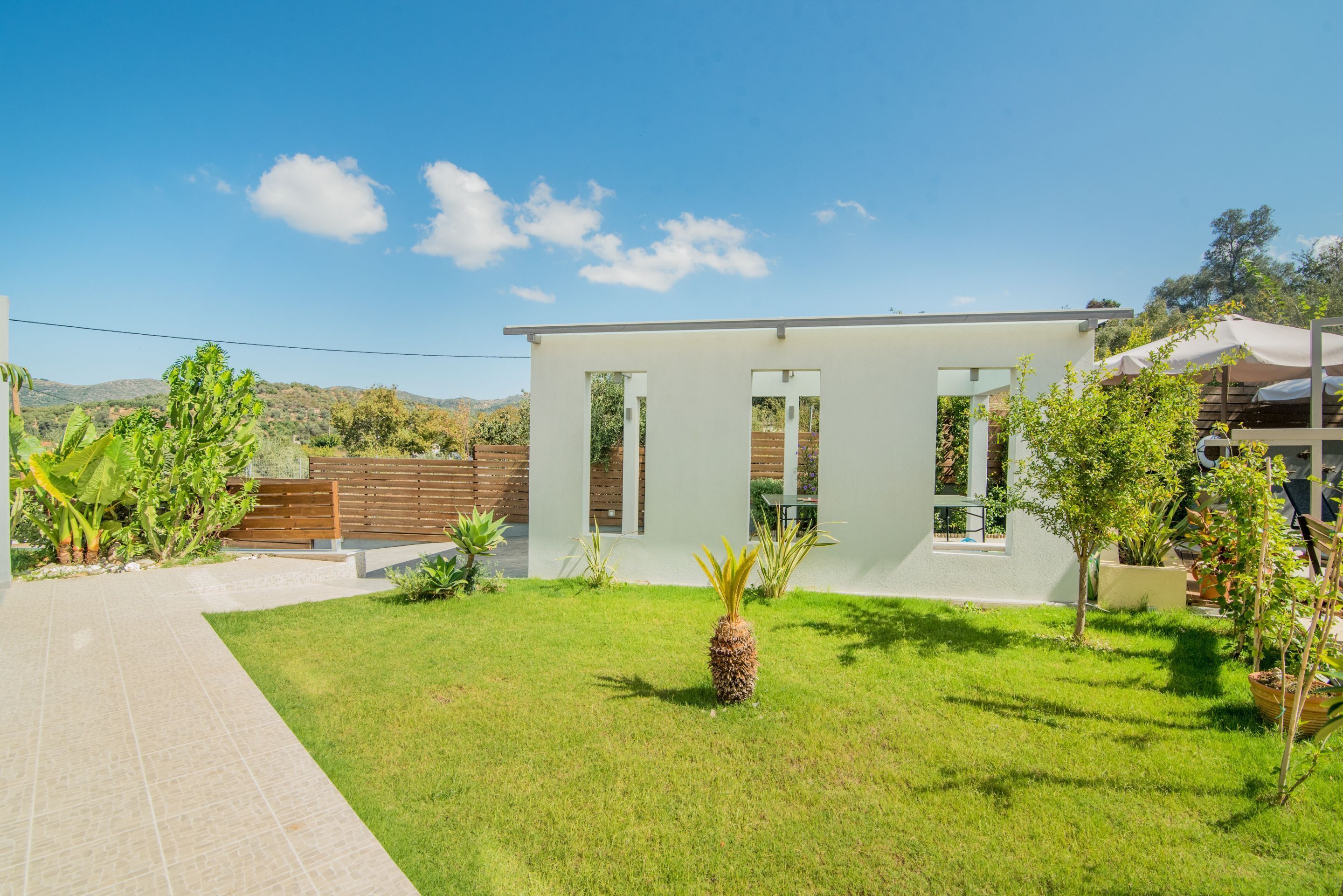 A modern house with a well-maintained lawn, a wooden fence, and a clear blue sky.
