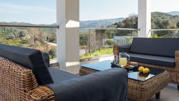 A balcony with wicker furniture, a glass table, and a view of the countryside. - Villa Alyona  (Platanias)