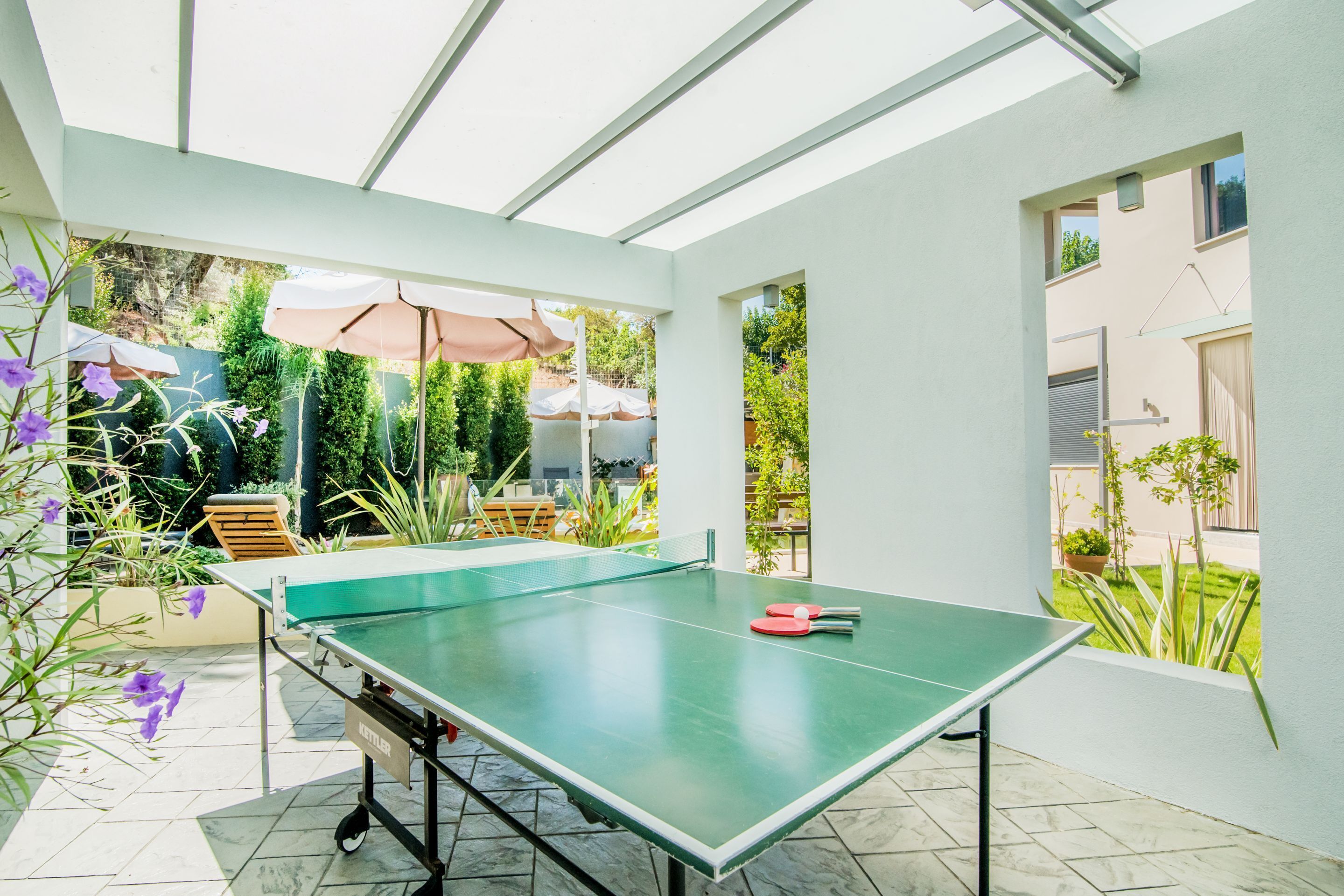 A ping pong table in a sunlit patio area with outdoor seating and umbrellas.