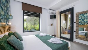 A modern bedroom with a large bed, green pillows, a view of greenery outside, a sliding glass door, and a mounted TV. - Villa Alyona  (Platanias)