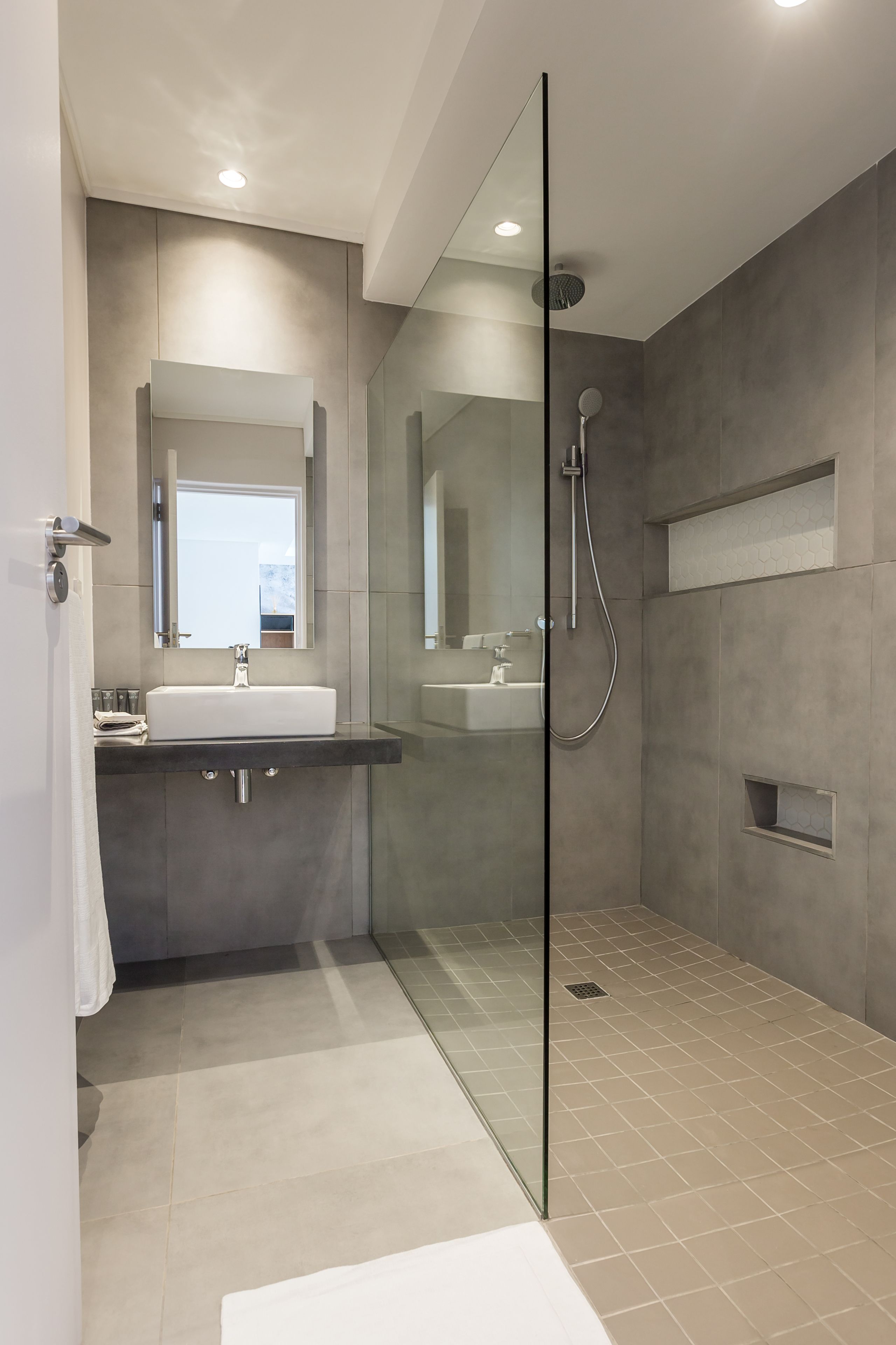 Een moderne badkamer met een douche met glazen wand, een grote spiegel en een wastafelmeubel met een wastafel.