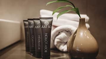 A bathroom with toiletries including shampoo, body wash, and lotion, a vase with a plant, and neatly folded towels.