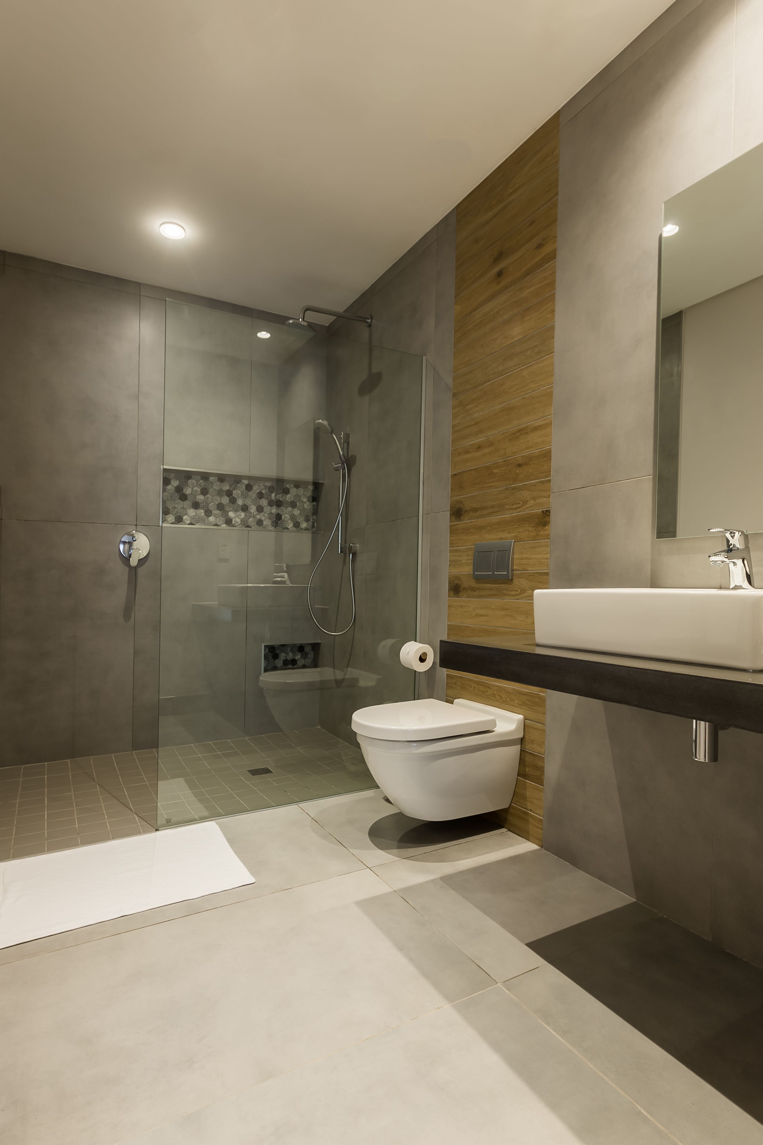 Une salle de bain moderne avec une douche à parois de verre, des toilettes blanches et un grand miroir au-dessus d’un plan de toilette foncé.