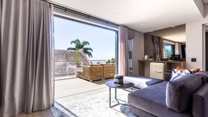 A modern living room with a sofa, a small round table, and a view of a balcony with outdoor furniture. - The Junction Boutique Hotel (Plettenberg Bay)