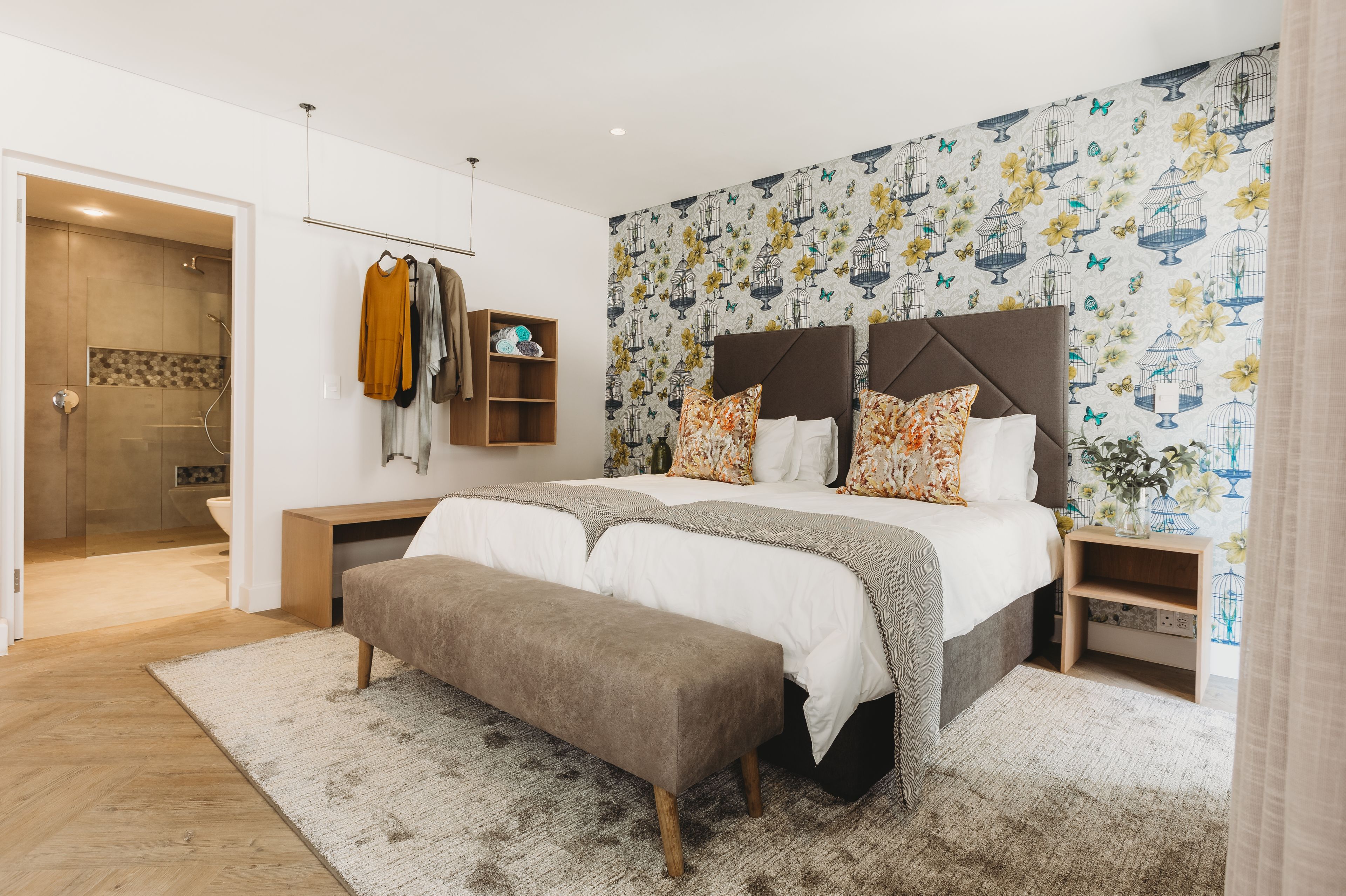 Un dormitorio moderno con una cama grande, un banco, un armario y una zona de ducha.