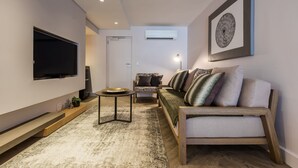 A modern living room with a flat-screen TV, a wooden sofa, a patterned armchair, and a coffee table. - The Junction Boutique Hotel (Plettenberg Bay)